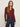 A woman with long brown hair wears the Sanctuary Clothing dreamgirl lace button up night berry shirt with high-waisted blue jeans, standing against a plain light background and gazing at the camera neutrally.