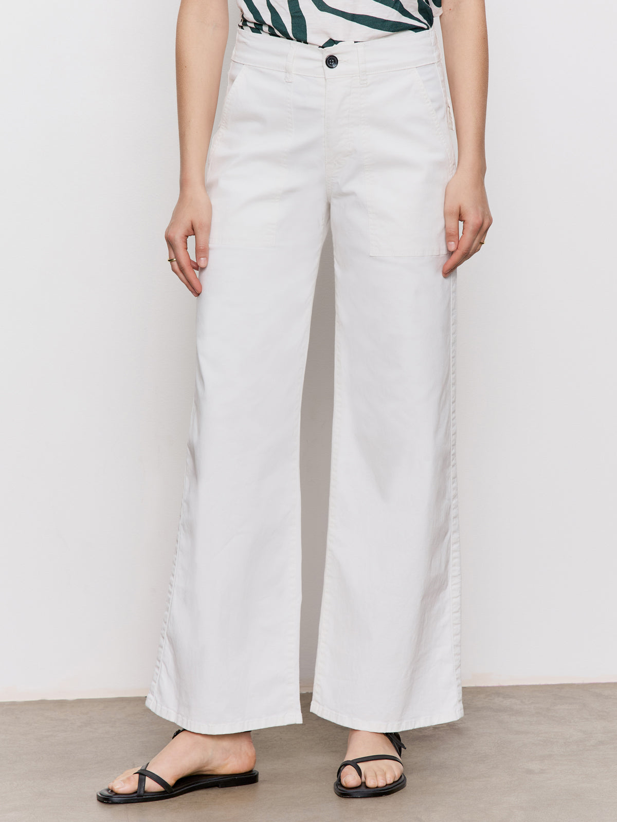 A person wears Sanctuary Clothing's cruiser full length powdered sugar pants, styled with a patterned top and black sandals, standing against a light background. The photo is cropped from the shoulders down.