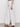 A person models the Sanctuary Clothing cruiser full length powdered sugar high-waisted, wide-leg pants and black sandals, standing against a plain background with their lower body visible and arm relaxed at their side.