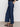 A person stands against a plain background wearing Sanctuary Clothing's league crop plot twist top, paired with wide-leg dark blue jeans and black sandals, with one hand in their back pocket.