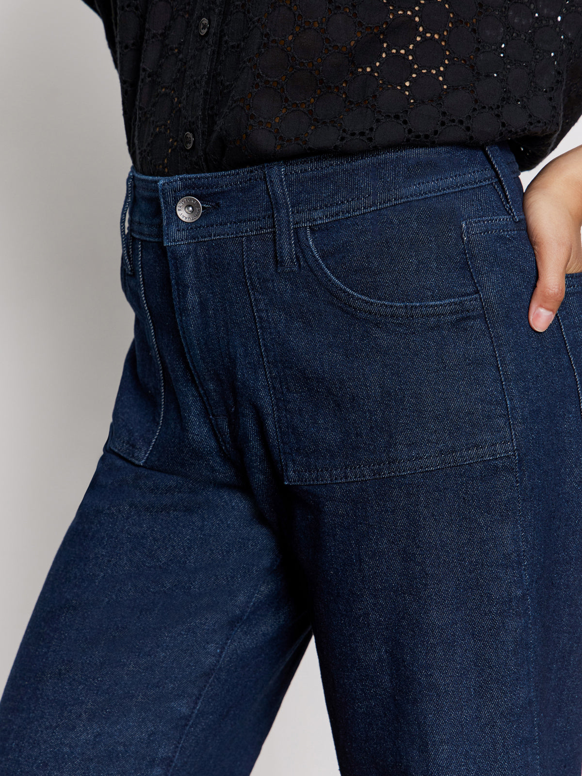 Wearing Sanctuary Clothing's league crop plot twist shirt, paired with high-waisted dark blue denim jeans featuring front patch pockets. The image shows the midsection and a hand resting on the hip.