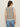 A woman with long brown hair, sunglasses, and blue jeans models the Sanctuary Clothing textured sweater vest macrame black stripe 3, standing with her back to the camera against a plain light background.
