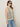 A woman stands in front of a plain light-colored background wearing Sanctuary Clothing's textured sweater vest macrame black stripe 3, sunglasses, and blue jeans.